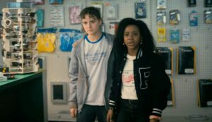 KJ Brandman in a t-shirt for the Stoney Creek Blubbers (baseball or softball) team. Tiffany Quilkin wears some Dave Matthews Band merchandise - Paper Girls