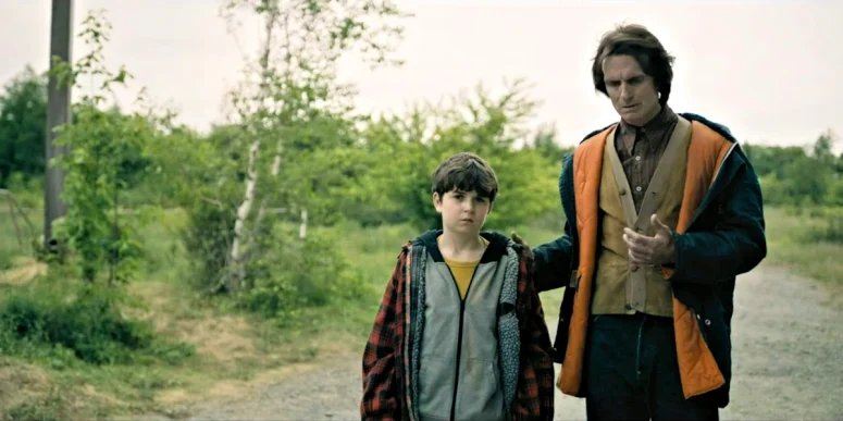 Victor (Scott McCord) and Ethan (Simon Webster) watch as Sophia and the pastor are taken to the clinic. Victor seems to pay sudden attention to his left hand. - From 401
