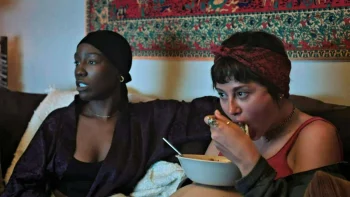 Sara (Chloe Van Landschoot) and Carol (Tymika Tafari) watch a zombie movie - Son of Sara