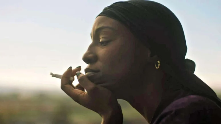 Carol (Tymika Tafari) pensively smokes a hand-rolled cigarette - Son of Sara